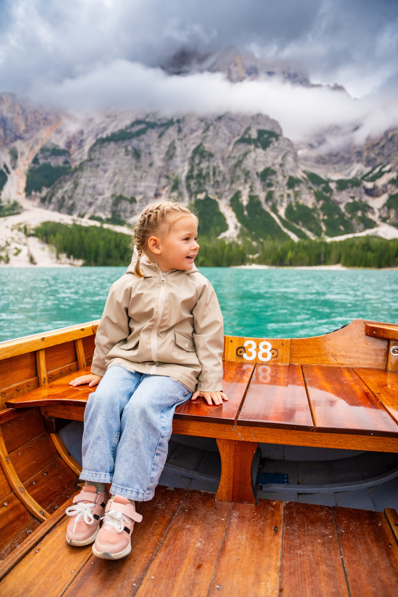 Little girl sitting in big brown boat at Lago di Braies lake in cloudy day, Italy. Summer vacation in Europe. High quality photo