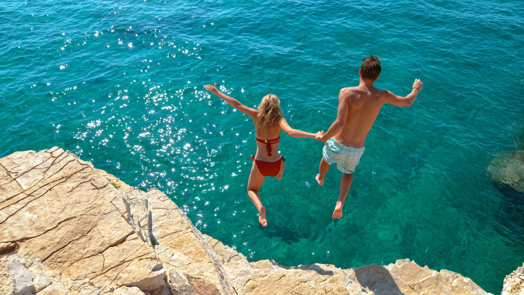Carefree,Tourists,Hold,Hands,While,Jumping,Into,The,Refreshing,Blue